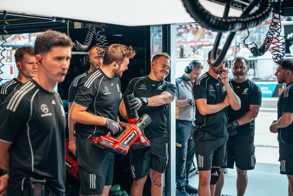 A equipe Mercedes-AMG PETRONAS Formula One Team está na garagem. Dois membros da equipe seguram sopradores sem fio vermelhos da Einhell e se preparam para a próxima ação.