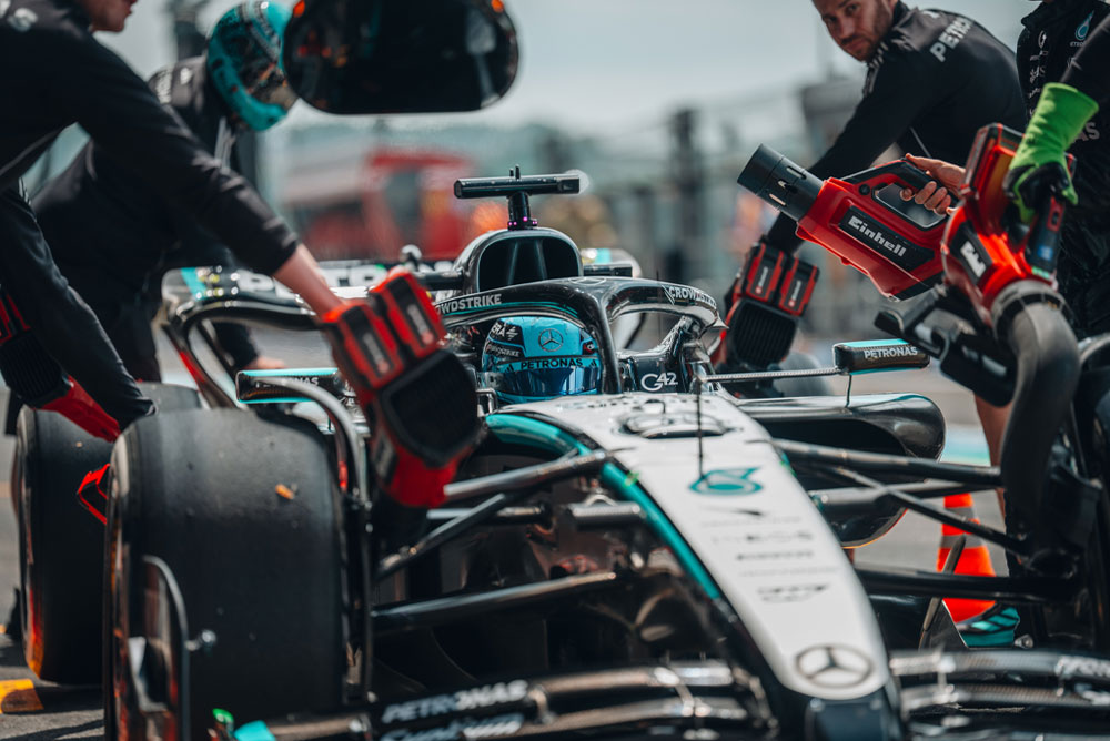 Um carro da Mercedes-AMG PETRONAS Formula One Team durante um pit stop. Os membros da equipe utilizam sopradores sem fio da Einhell para resfriar os componentes do veículo. A equipe está concentrada e trabalha com precisão.