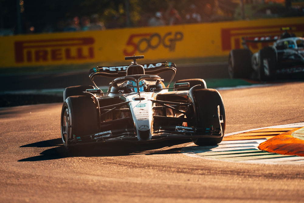 Um carro da Mercedes-AMG PETRONAS Formula One Team corre em uma pista ensolarada durante um Grande Prêmio. O carro faz uma curva em alta velocidade, com outro carro visível ao fundo.