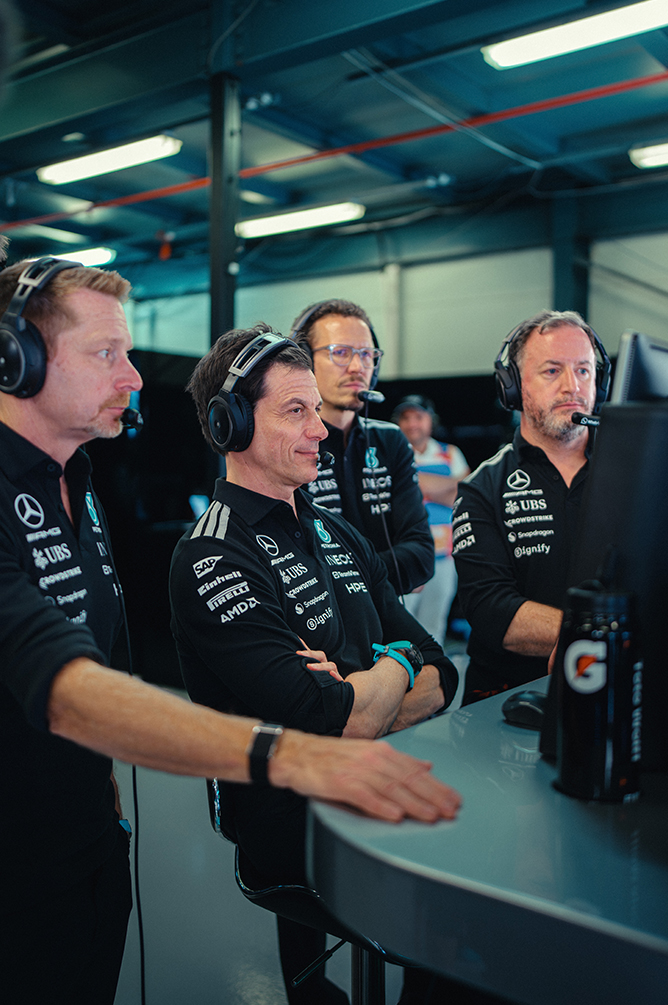 Membros da equipe de Fórmula 1 com fones monitorando a corrida do pit wall.