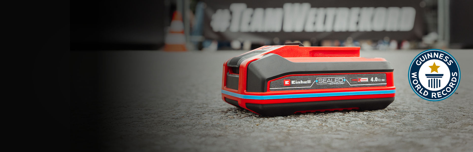 A bateria Einhell SEALED Power X-Change 4.0 Ah está sobre o asfalto, com o logótipo "Record Holder" do Guinness World Records à direita.