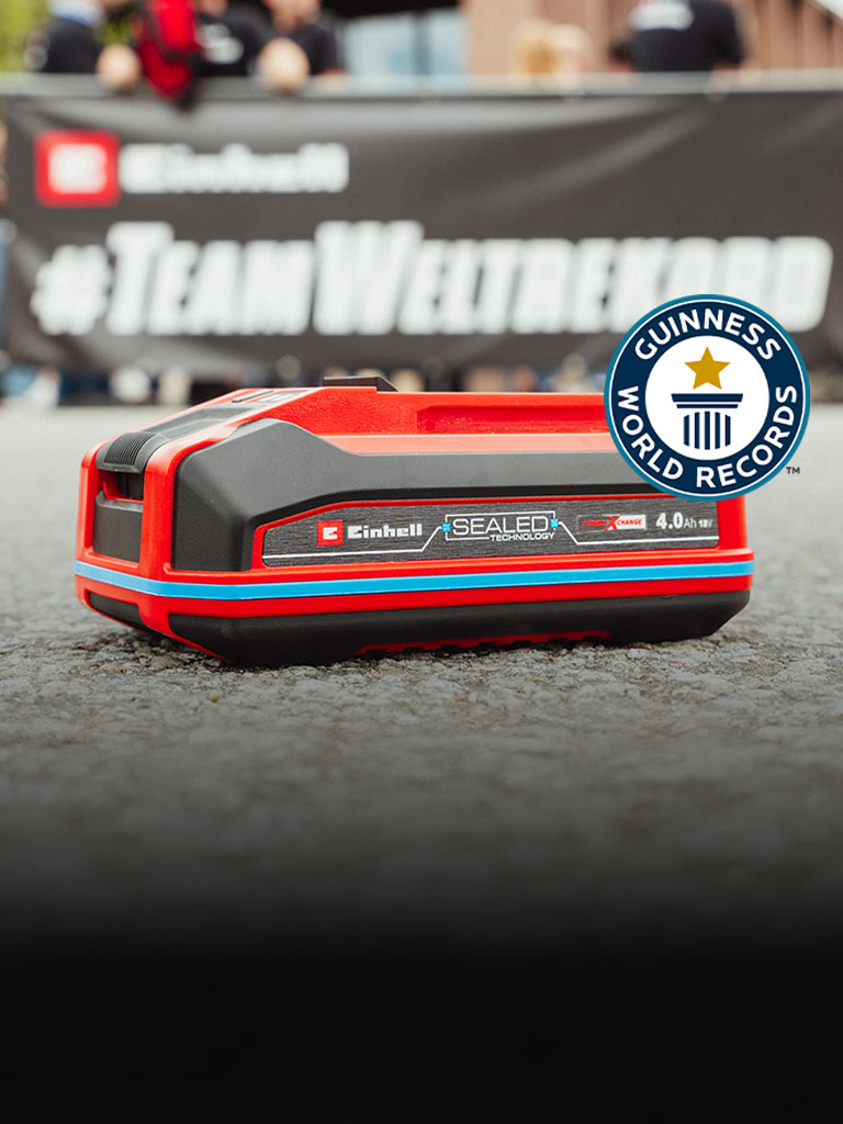 A bateria Einhell SEALED Power X-Change 4.0 Ah está sobre o asfalto, com o logótipo "Record Holder" do Guinness World Records à direita.