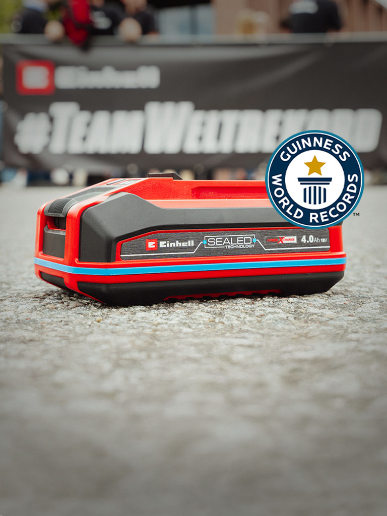 A bateria Einhell SEALED Power X-Change 4.0 Ah está sobre o asfalto, com o logótipo "Record Holder" do Guinness World Records à direita.