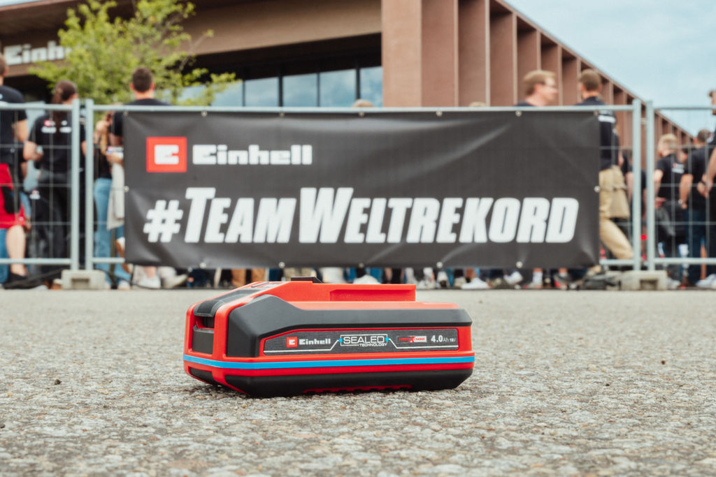 Akumulátor Einhell SEALED Power X-Change 4,0 Ah leží na asfaltu, vpravo logo Guinness World Records „Record Holder“.