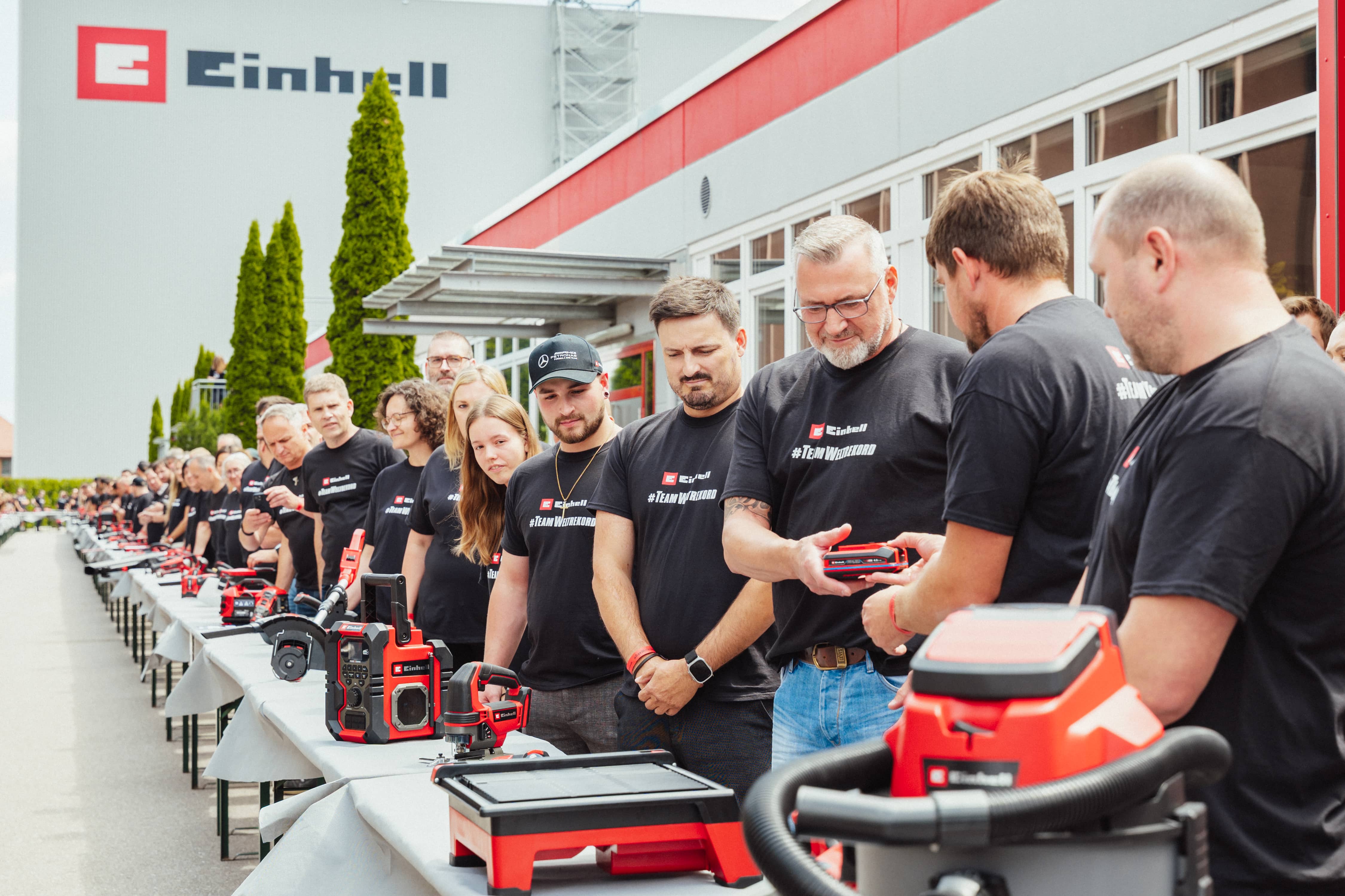 Colaboradores da Einhell estão junto a mesas com ferramentas e passam uma bateria SEALED.